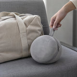 The neck pillow packed into its round grey case beside a canvas weekend bag