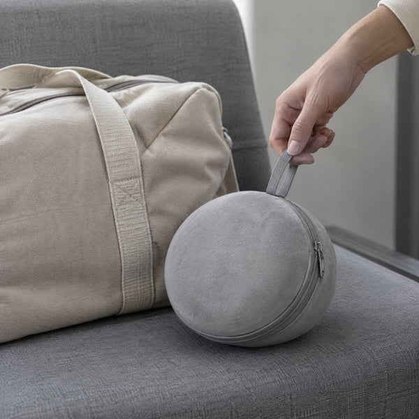The neck pillow packed into its round grey case beside a canvas weekend bag